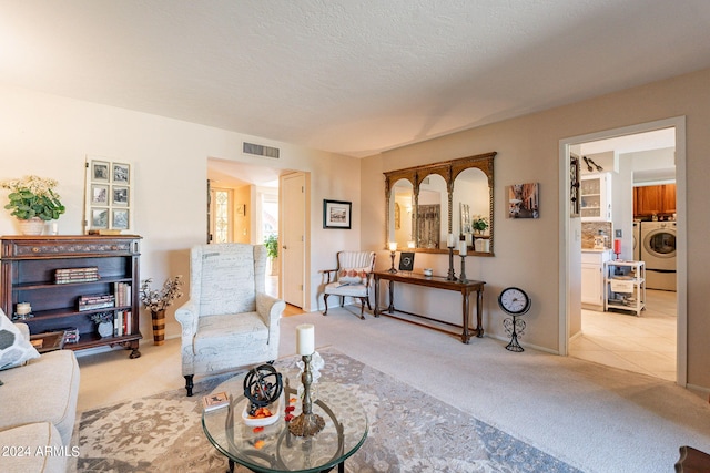 living room with a textured ceiling, washer / clothes dryer, and light colored carpet