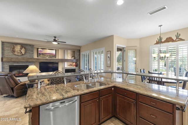 kitchen with a fireplace, dishwasher, sink, pendant lighting, and light stone counters