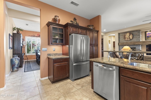 kitchen featuring appliances with stainless steel finishes, sink, dark stone counters, light tile patterned floors, and dark brown cabinetry