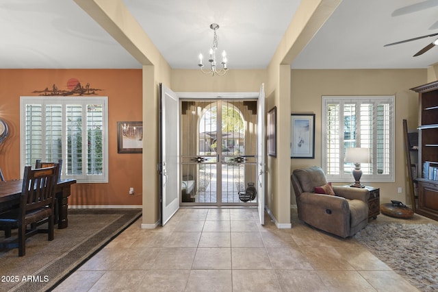 foyer entrance with ceiling fan with notable chandelier, light tile patterned floors, and plenty of natural light