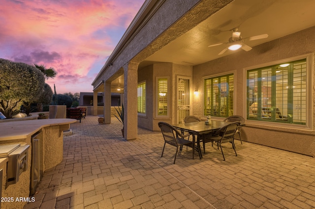 patio terrace at dusk featuring exterior bar and ceiling fan