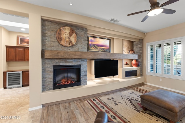 unfurnished living room featuring ceiling fan, beverage cooler, light wood-type flooring, and a fireplace