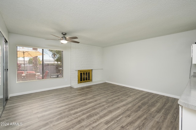 unfurnished living room with a brick fireplace, wood-type flooring, ceiling fan, and a textured ceiling