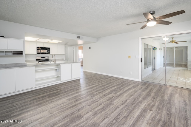 kitchen featuring light wood-type flooring, a textured ceiling, stainless steel range with electric cooktop, white cabinetry, and ceiling fan