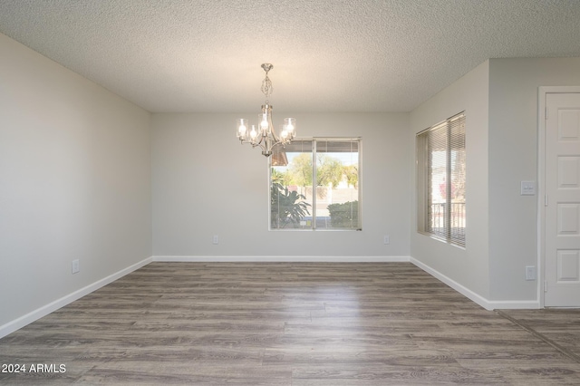 empty room featuring an inviting chandelier, a textured ceiling, baseboards, and wood finished floors