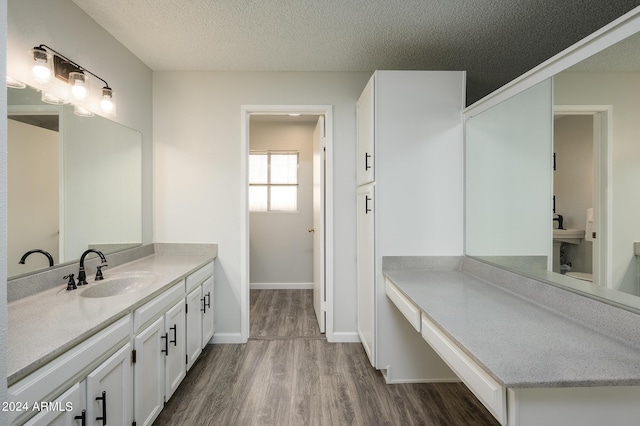 bathroom with a textured ceiling, wood finished floors, vanity, and baseboards