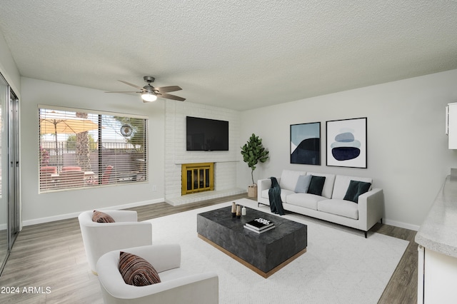 living room with a textured ceiling, ceiling fan, a brick fireplace, and hardwood / wood-style flooring