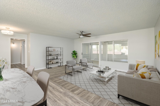 living area with light wood-type flooring, ceiling fan, baseboards, and a textured ceiling