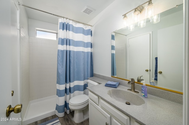 bathroom with visible vents, toilet, vanity, wood finished floors, and tiled shower