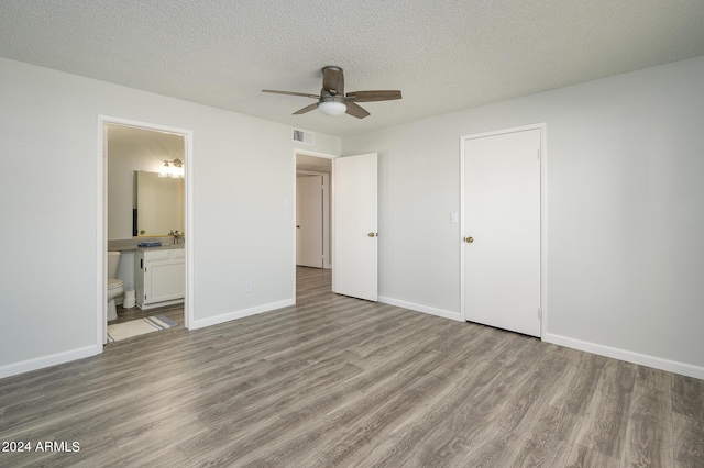 unfurnished bedroom featuring visible vents, connected bathroom, a textured ceiling, wood finished floors, and baseboards