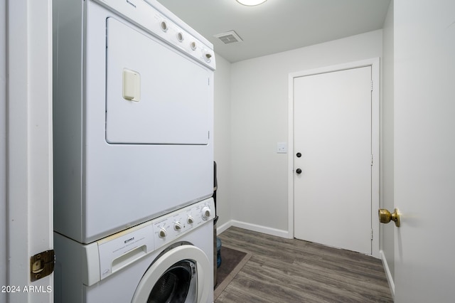 clothes washing area featuring stacked washer and clothes dryer, visible vents, wood finished floors, laundry area, and baseboards