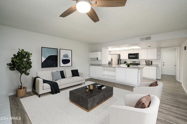 living room with light wood-type flooring, a textured ceiling, and ceiling fan