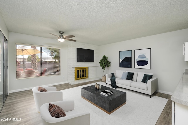 living room featuring a textured ceiling, ceiling fan, baseboards, light wood-type flooring, and a brick fireplace