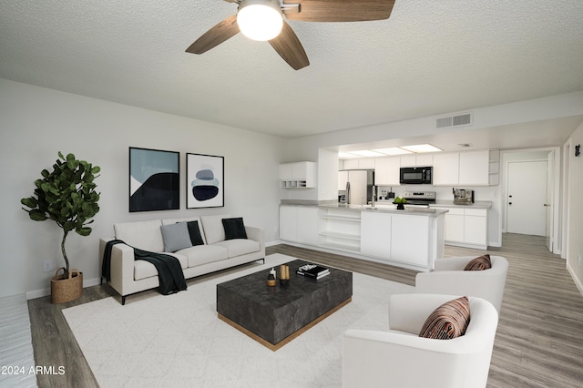 living area with light wood-style floors, visible vents, a textured ceiling, and baseboards