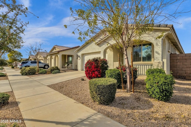 mediterranean / spanish house with concrete driveway, a tiled roof, an attached garage, fence, and stucco siding