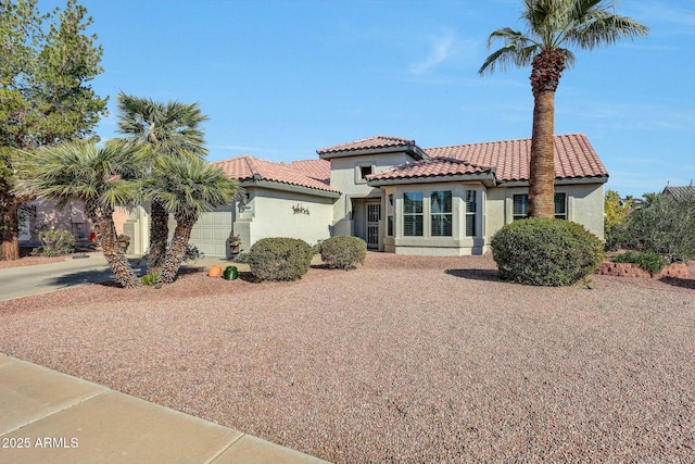 mediterranean / spanish house featuring a tiled roof, an attached garage, driveway, and stucco siding