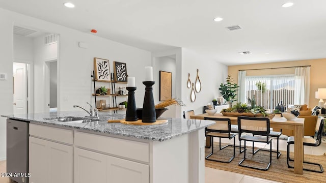 kitchen with light stone counters, visible vents, a sink, white cabinetry, and open floor plan