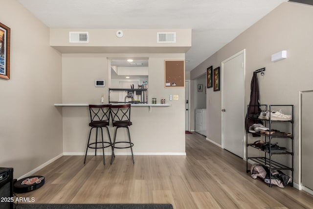 kitchen with light wood-type flooring, visible vents, and a breakfast bar