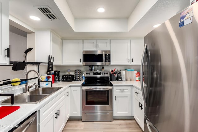 kitchen featuring appliances with stainless steel finishes, white cabinets, visible vents, and a sink