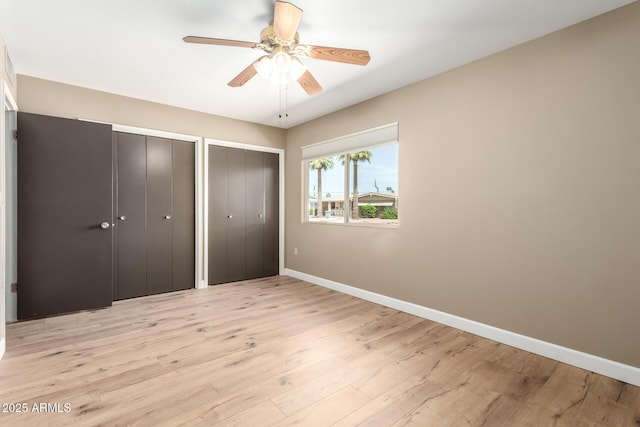 unfurnished bedroom with baseboards, a ceiling fan, light wood-style flooring, and two closets