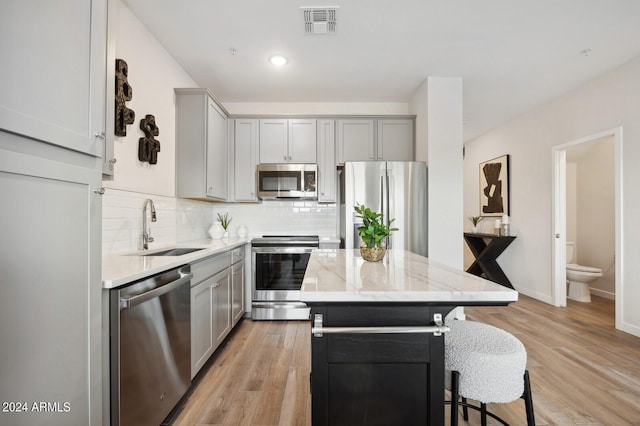 kitchen with sink, a center island, light stone counters, light hardwood / wood-style floors, and appliances with stainless steel finishes