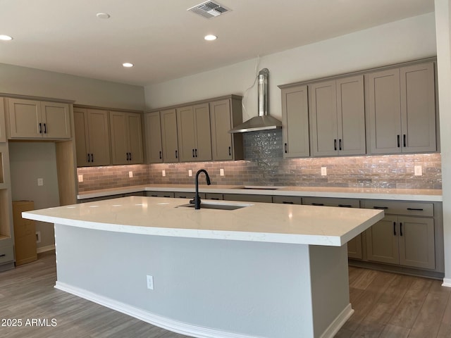 kitchen featuring light stone countertops, an island with sink, and wall chimney range hood