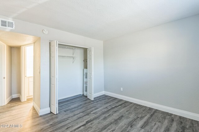 unfurnished bedroom with a textured ceiling, electric water heater, hardwood / wood-style flooring, and a closet