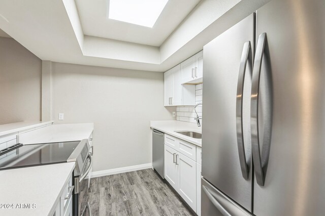 kitchen featuring tasteful backsplash, white cabinetry, a tray ceiling, light hardwood / wood-style floors, and stainless steel appliances