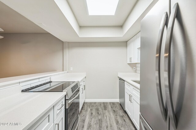 kitchen featuring appliances with stainless steel finishes, light hardwood / wood-style flooring, white cabinetry, and a raised ceiling