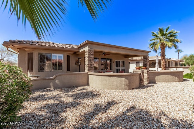 rear view of house with stone siding, stucco siding, a patio, and a ceiling fan