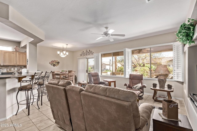 living room featuring baseboards, light tile patterned flooring, and ceiling fan with notable chandelier