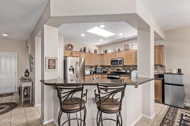 kitchen with a kitchen bar, dark countertops, a skylight, and appliances with stainless steel finishes