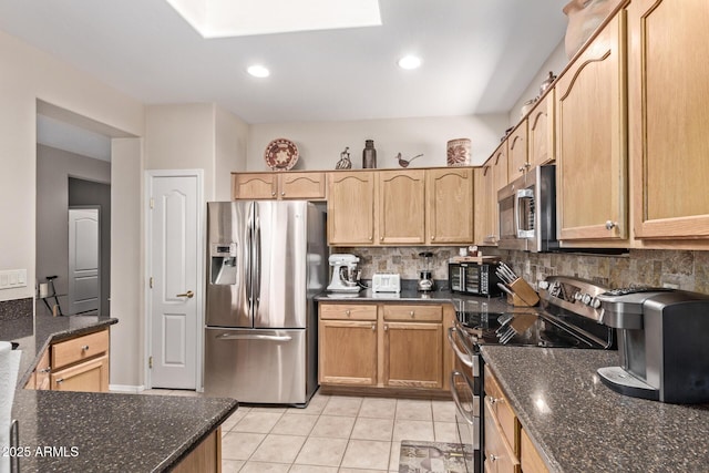 kitchen with tasteful backsplash, dark stone countertops, appliances with stainless steel finishes, and a skylight