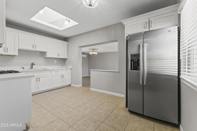 kitchen featuring sink, a skylight, stainless steel fridge with ice dispenser, light tile patterned floors, and white cabinets