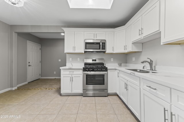 kitchen featuring sink, a skylight, light tile patterned floors, stainless steel appliances, and white cabinets