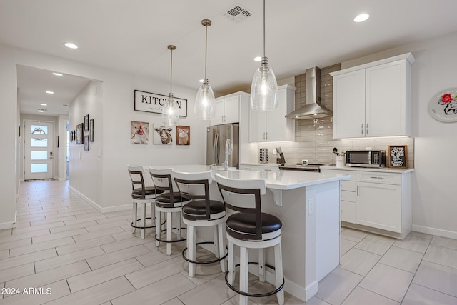 kitchen with white cabinets, an island with sink, stainless steel appliances, and wall chimney range hood