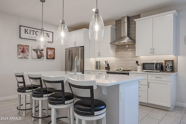 kitchen featuring white cabinetry, wall chimney exhaust hood, stainless steel appliances, tasteful backsplash, and a kitchen island with sink