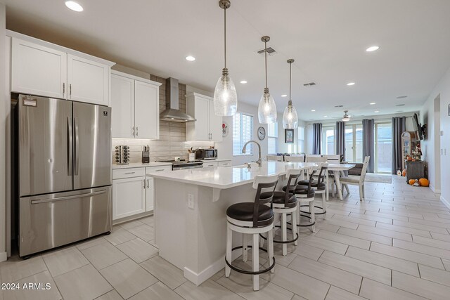 kitchen with plenty of natural light, a center island with sink, stainless steel appliances, and wall chimney range hood