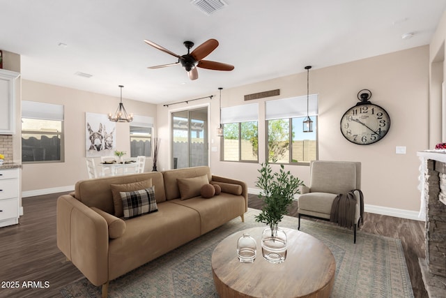 living room featuring visible vents, a stone fireplace, baseboards, ceiling fan, and dark wood-style flooring