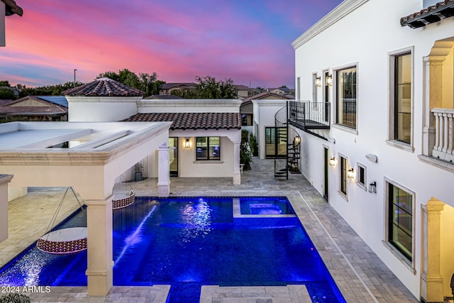 pool at dusk with an in ground hot tub and a patio