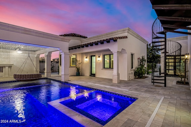 pool at dusk with an in ground hot tub and a patio