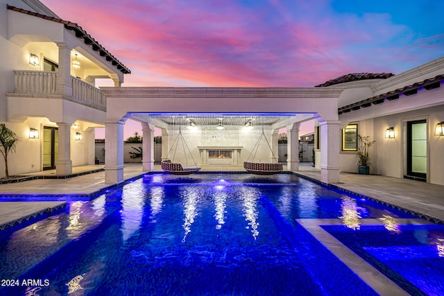 pool at dusk featuring a patio area and an in ground hot tub