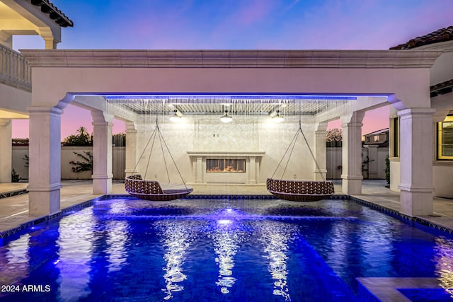 pool at dusk featuring a patio and exterior fireplace