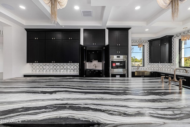 kitchen with beam ceiling, stainless steel double oven, tasteful backsplash, and a healthy amount of sunlight