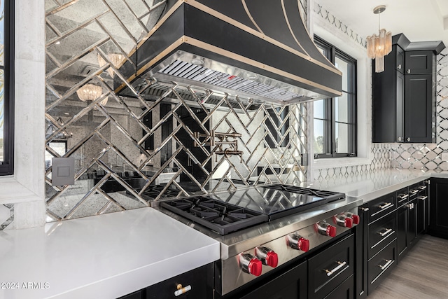 kitchen featuring light hardwood / wood-style flooring, premium range hood, backsplash, decorative light fixtures, and stainless steel gas stovetop