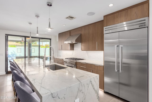 kitchen featuring pendant lighting, a kitchen island with sink, high quality appliances, and range hood