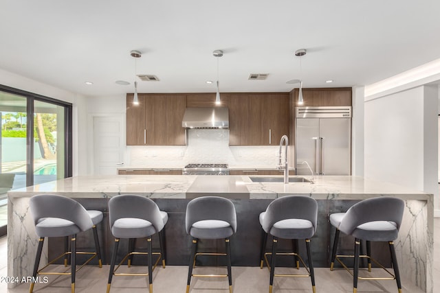 kitchen featuring sink, decorative light fixtures, appliances with stainless steel finishes, a kitchen breakfast bar, and range hood