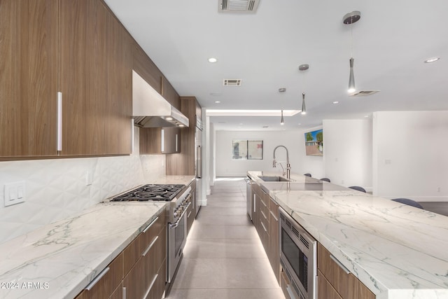 kitchen featuring sink, decorative light fixtures, backsplash, wall chimney range hood, and appliances with stainless steel finishes