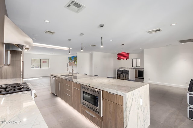 kitchen with extractor fan, a large island with sink, sink, light stone counters, and stainless steel appliances