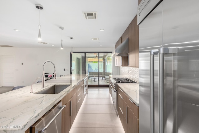 kitchen with tasteful backsplash, ventilation hood, high quality appliances, decorative light fixtures, and sink